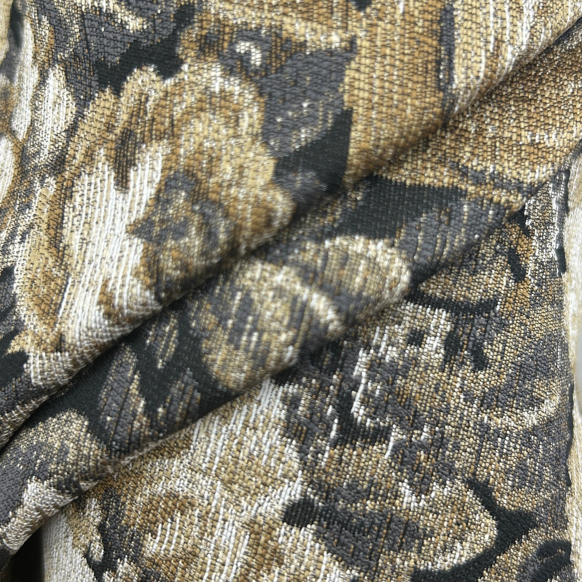 A close-up of draped fabric with a woven floral pattern in beige, brown, black, and off-white tones.
