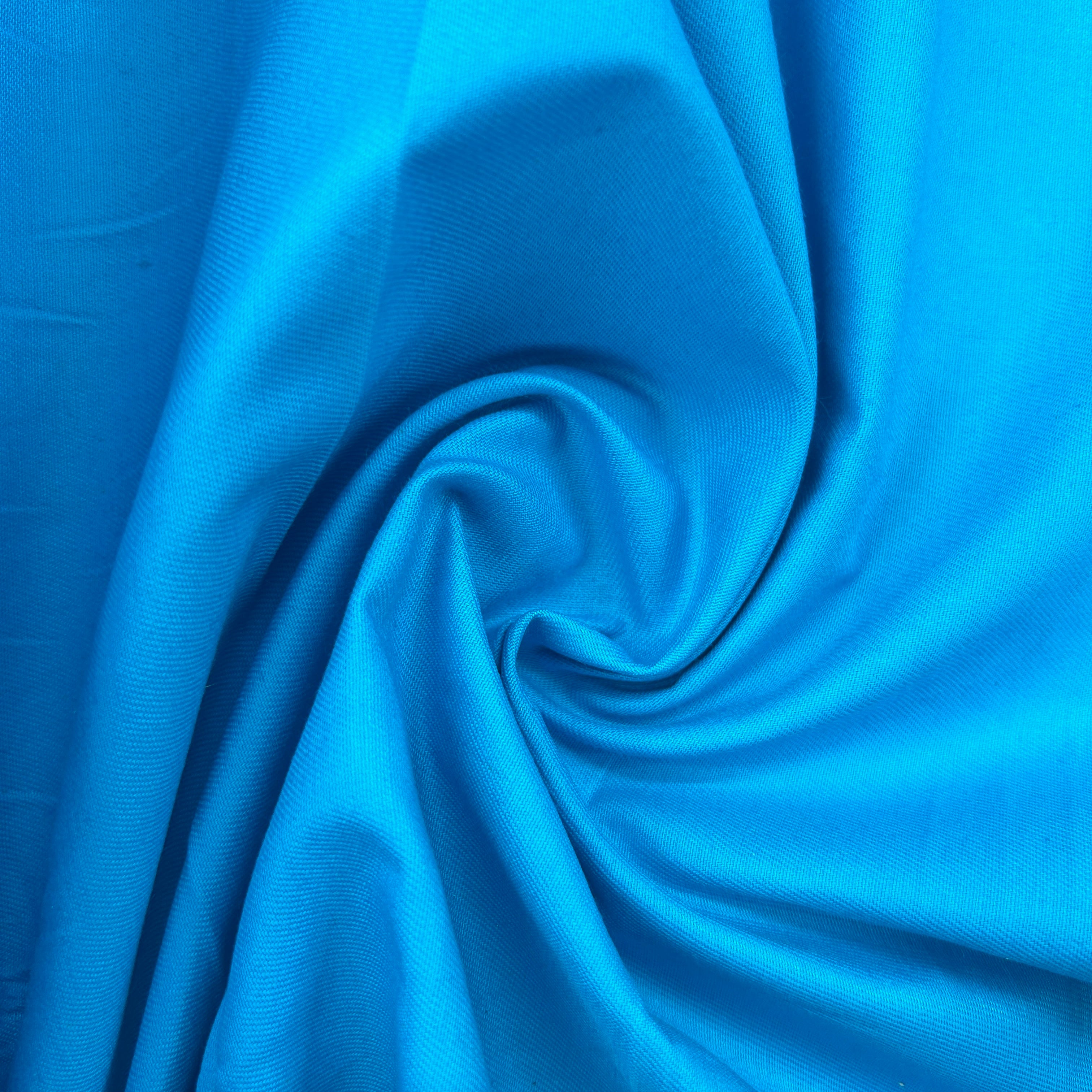 A close-up of bright blue fabric draped in a spiral pattern, showing its smooth texture and sheen.