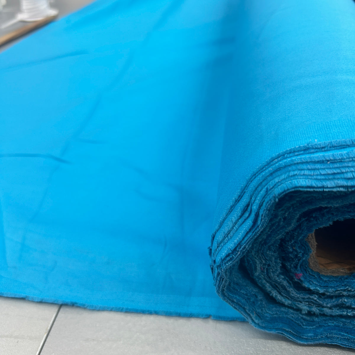 A bright blue roll of fabric or material partially unrolled, showing its woven texture and layered edges, set against a light gray tiled floor.