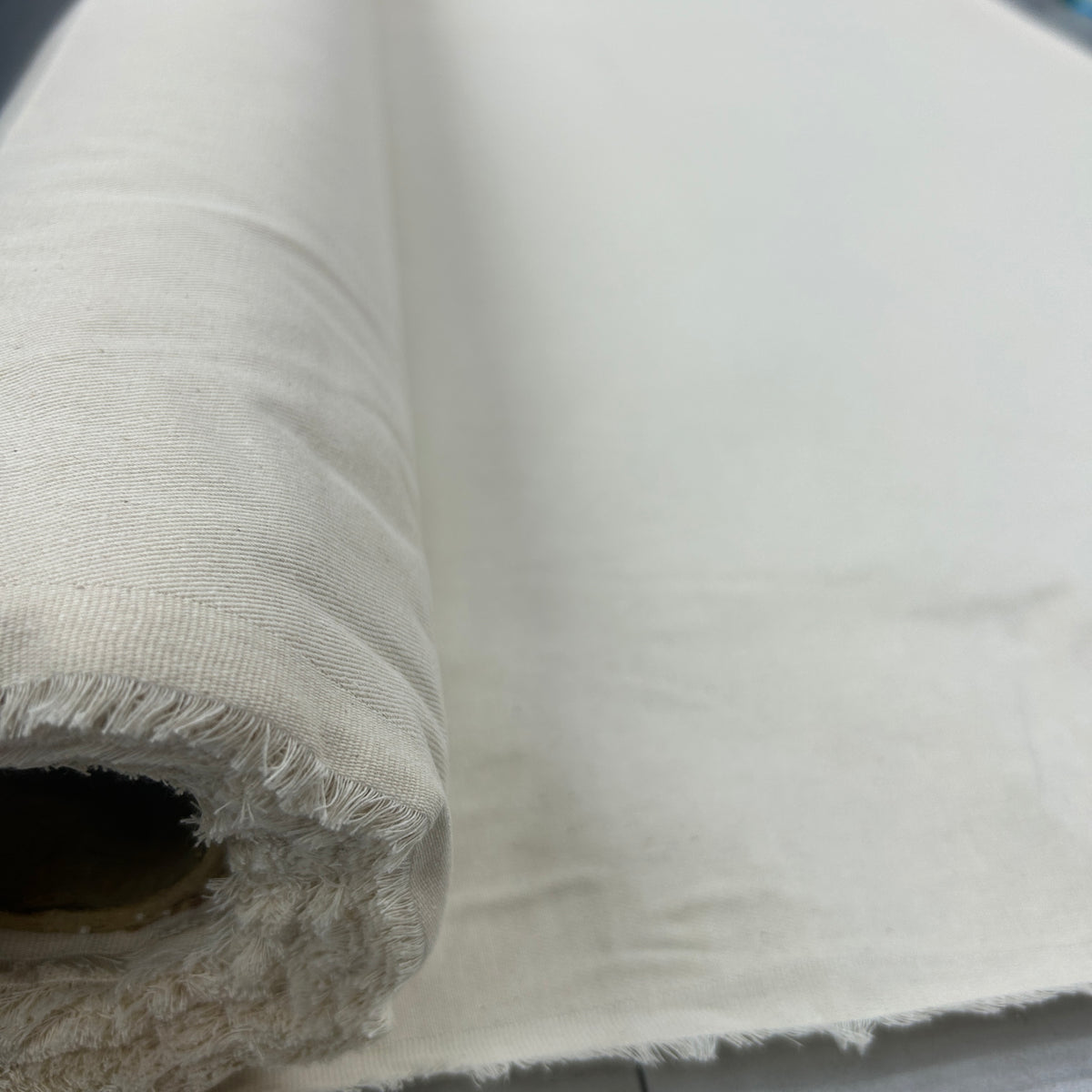 A close-up of a rolled piece of off-white or cream-colored fabric, showing its woven texture and frayed edges.