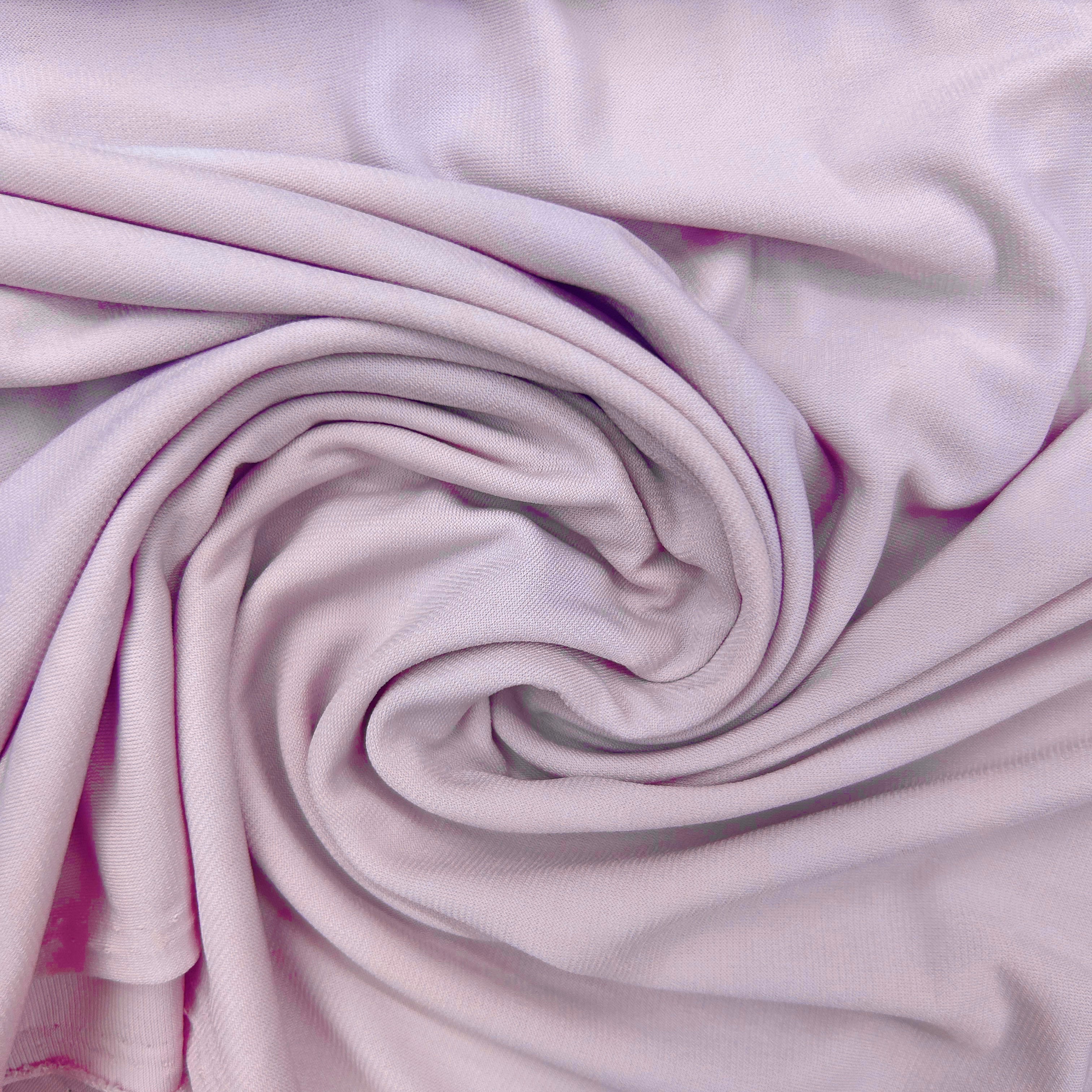 A close-up of light pink fabric arranged in a spiral drape, showing the material texture and soft folds.