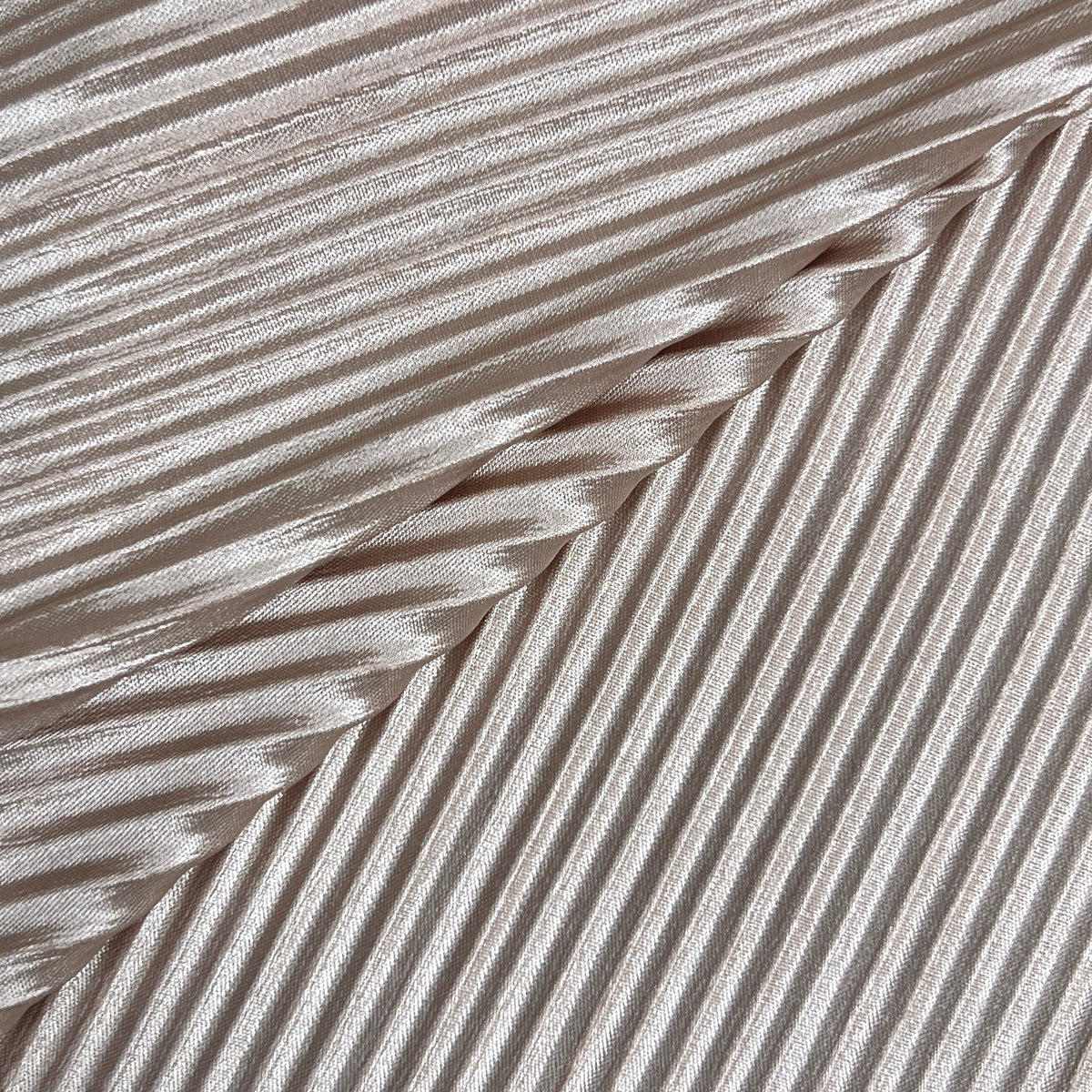 A close-up of a pleated fabric with diagonal rows and a subtle sheen, shown in a light champagne or beige tone.