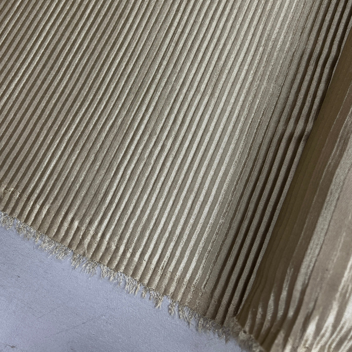 A close-up of a beige ribbed fabric with a frayed edge, laid diagonally across a light gray surface.