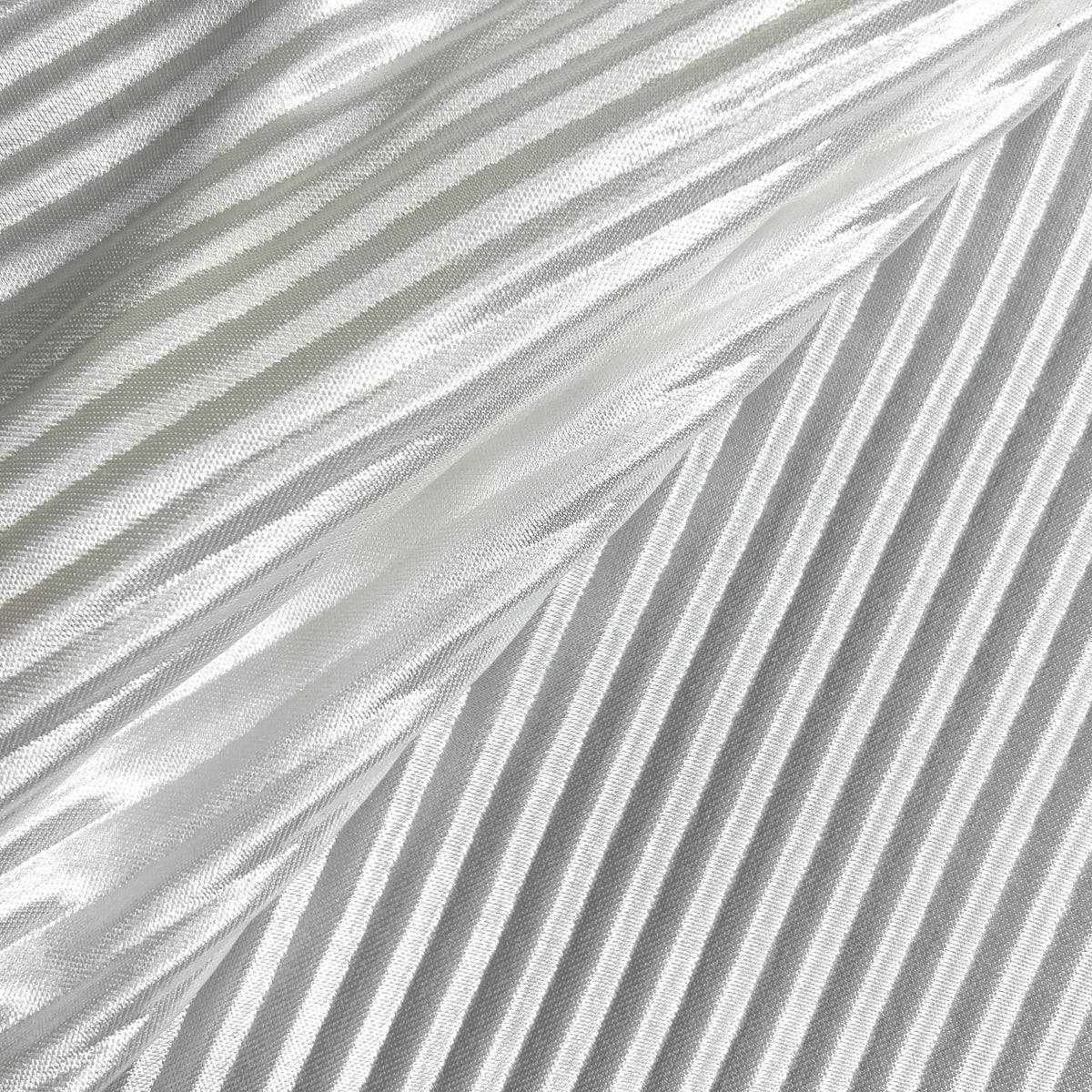A close-up of a white pleated fabric with diagonal pleats, draped diagonally across the frame against a neutral gray background.