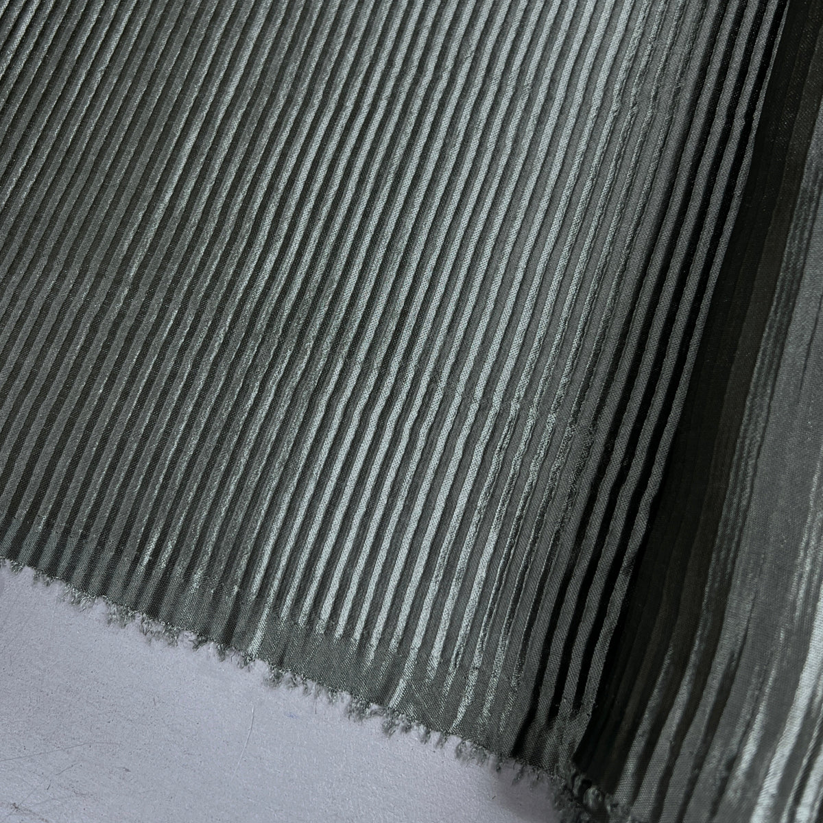 A close-up of a ribbed gray material, likely a textured fabric, wallpaper, or adhesive vinyl sheet, with a white surface visible in the bottom-left corner.