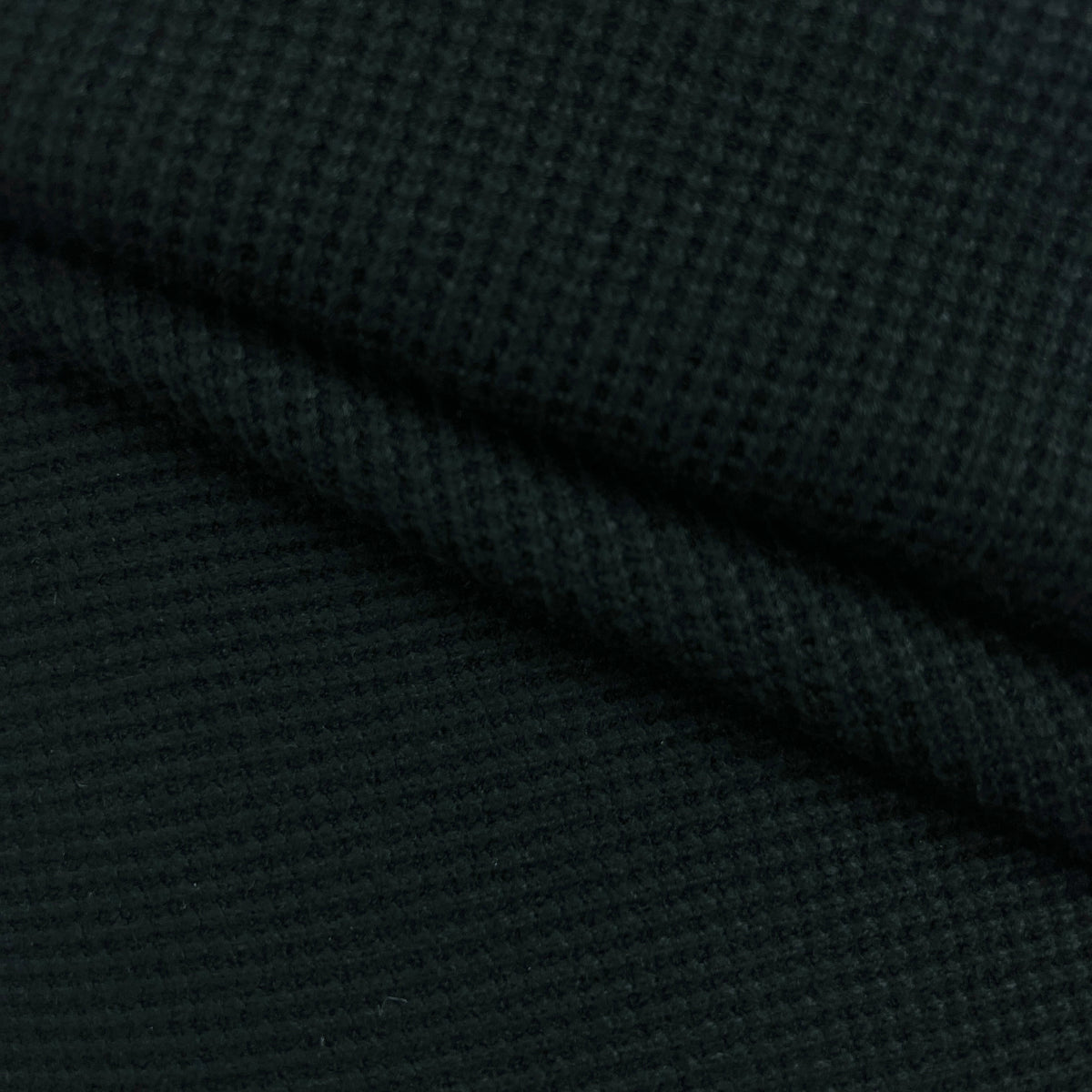 A close-up of dark charcoal gray waffle knit fabric with a textured grid pattern and soft folds.
