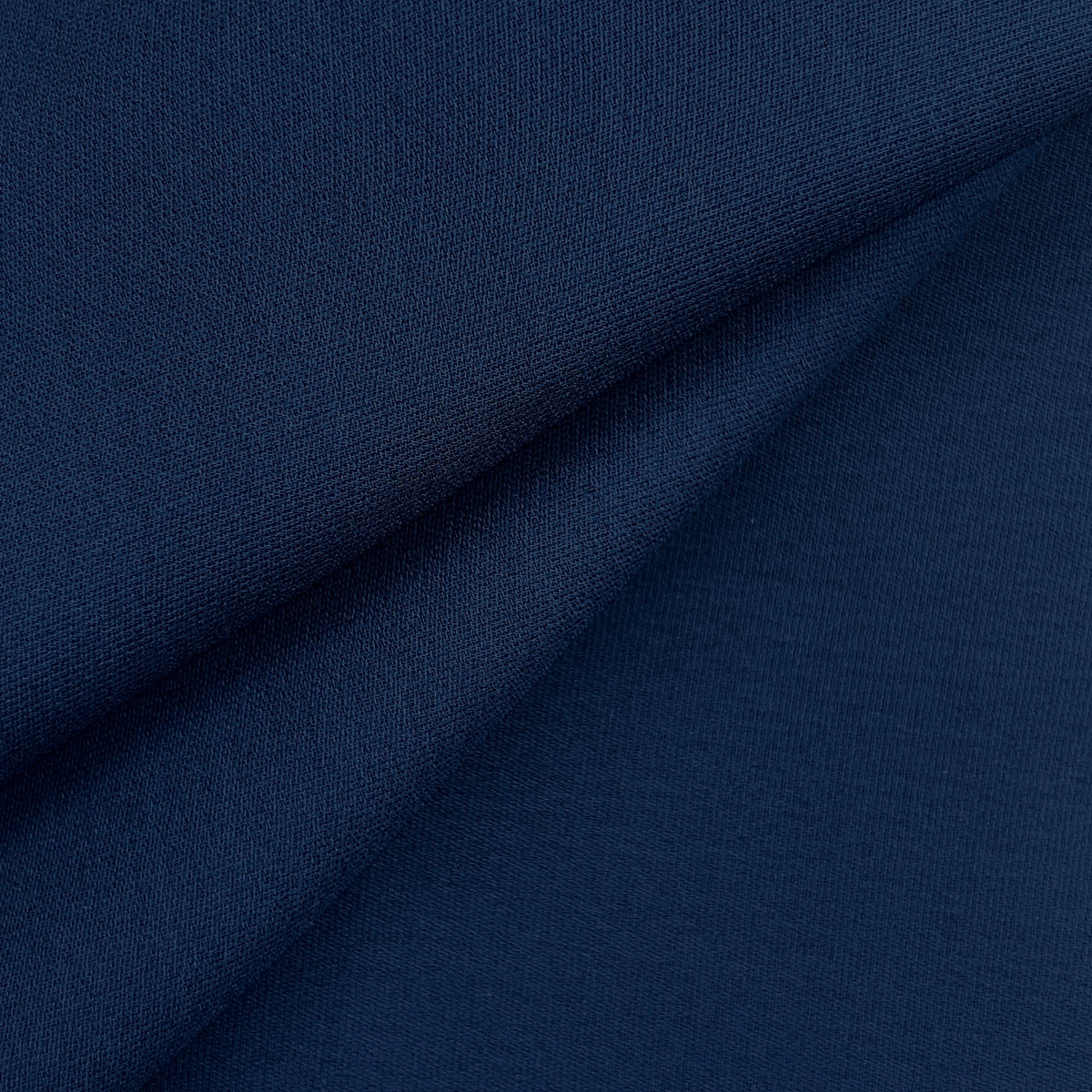 A close-up of dark navy blue knit fabric with soft diagonal folds showing the texture and color.