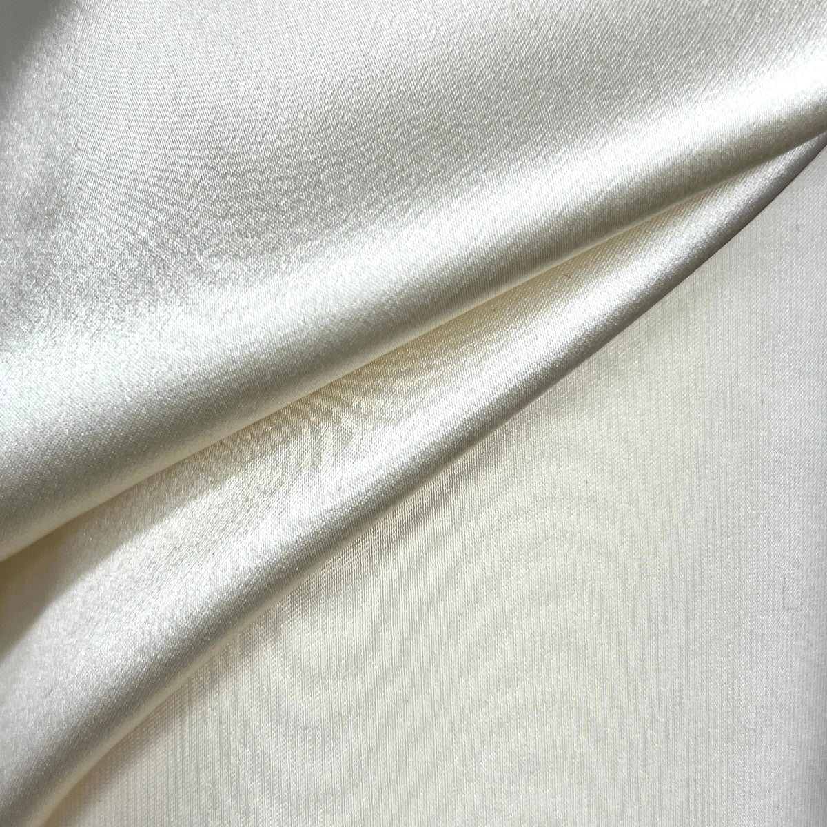 A close-up of draped satin fabric in a warm ivory or cream color, showing its smooth texture and soft sheen.