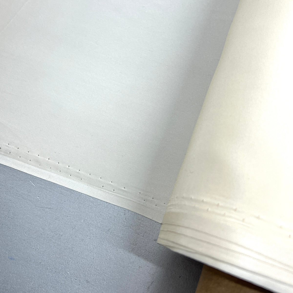 A close-up of a white fabric or material roll laid over a gray surface, with the rolled edge visible on the right side.
