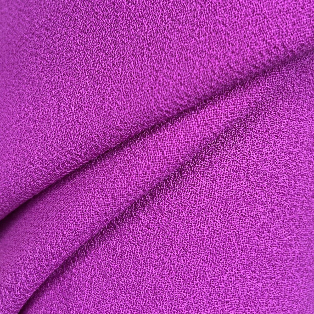 A close-up of draped purple fabric with a textured woven surface, showing folds and a light neutral background.