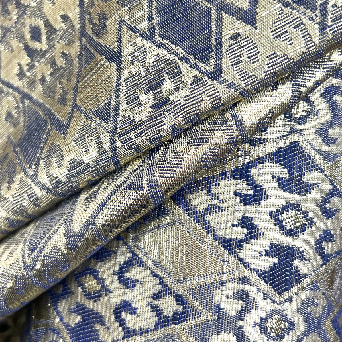 A close-up of a folded woven fabric with an intricate geometric and floral pattern in navy blue, beige, and gray.