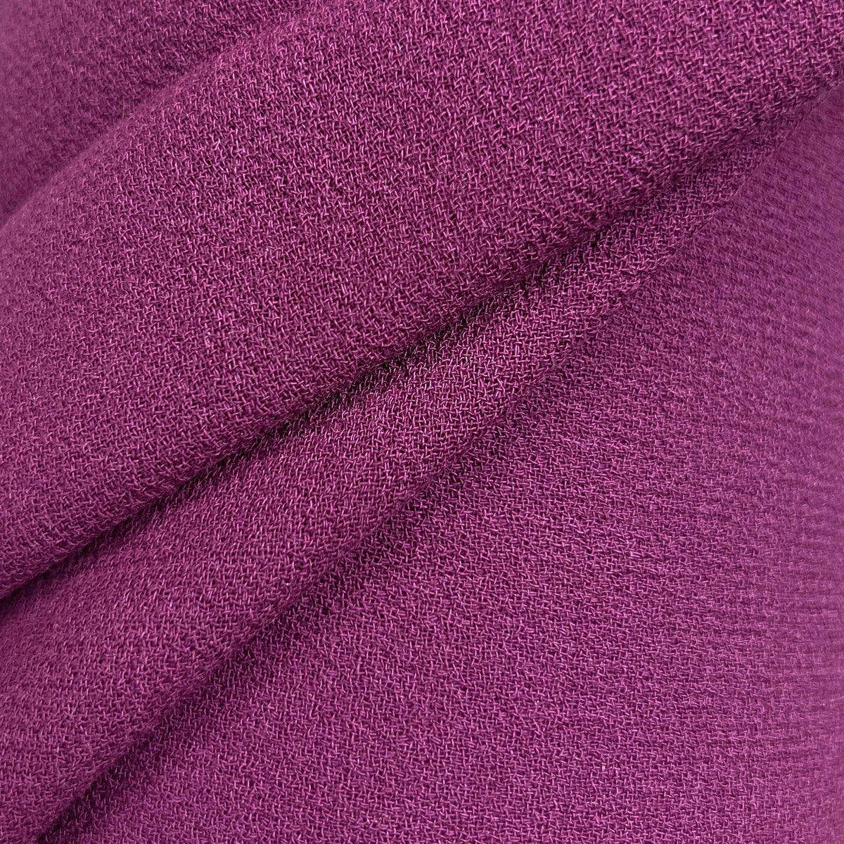 A close-up of draped purple fabric with a textured, woven surface against a white background.